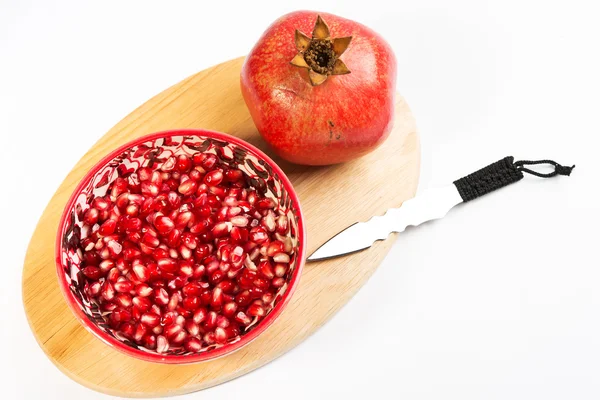 Loose pomegranate (Punica granatum) seeds in a red bowl shot on a wood cutting board. isolated on white background — Stock Photo, Image