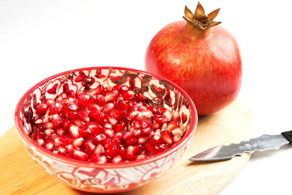 Semillas de granada suelta (Punica granatum) en un tazón rojo sobre una tabla de cortar madera. aislado sobre fondo blanco — Foto de Stock