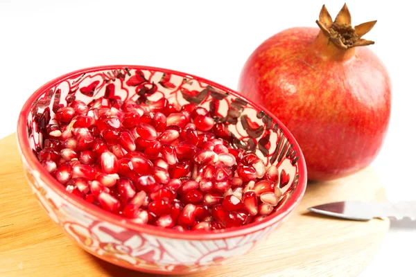 Lös granatäpplekärnor (Punica granatum) i en röd skål skott på en trä skärbräda. isolerad på vit bakgrund — Stockfoto