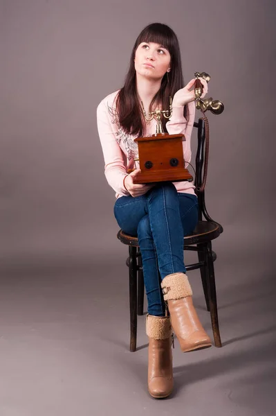 Young attractive woman sits on chair with vintage phone over grey background