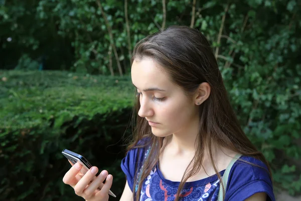 Chica con un teléfono móvil lee el mensaje en el parque —  Fotos de Stock