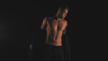 Siyah arkaplanda siyah hırkalı seksi bir adam.