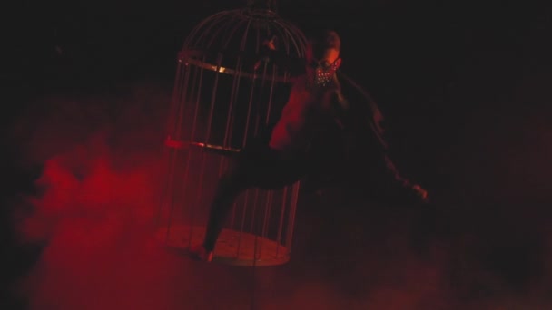 Человек в маске в красном свете в дыму танцует — стоковое видео