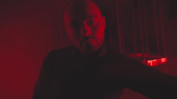 Άνδρας με μαύρο σε κόκκινο φως στον καπνό κοντά στο μεταλλικό κλουβί — Αρχείο Βίντεο