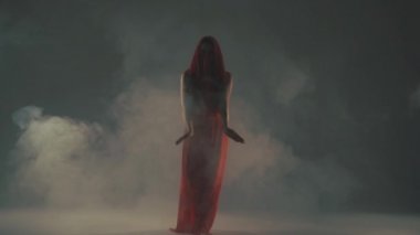 Kırmızı elbiseli kadın duman içinde dans ediyor.
