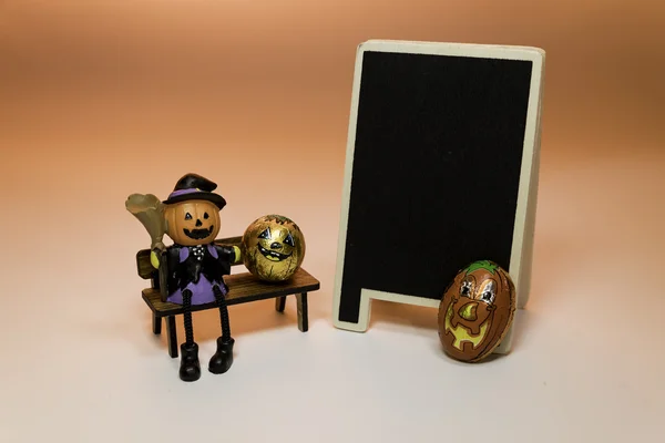 Halloween Pumpkin doll sit on the bench near blackboard — Stock Photo, Image