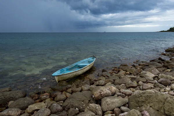 Kleine boot op rots strand met regen storm — Stockfoto