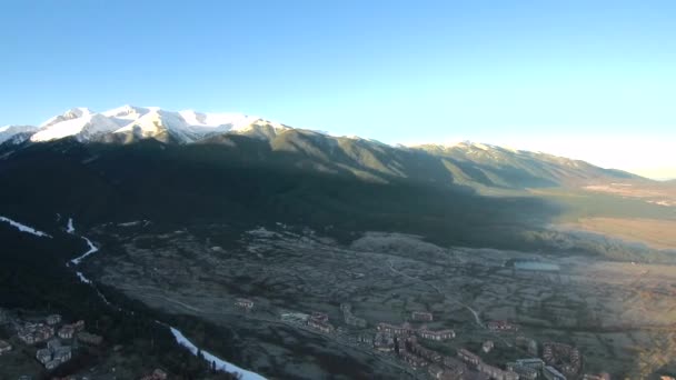 Nagrania z lotu ptaka nad wioską w słoneczny poranek ze śnieżnymi górami na horyzoncie — Wideo stockowe