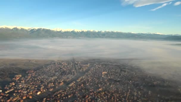 Nagrania z lotu ptaka nad wioską w słoneczny poranek ze śnieżnymi górami na horyzoncie — Wideo stockowe