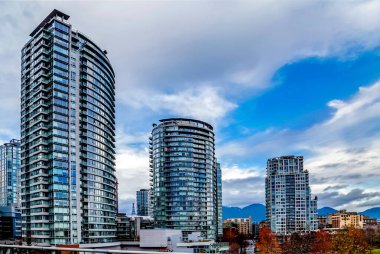 Sonbaharda Vancouver şehir merkezinin mimari parçası, sokakta sarı ağaçlar dağ sırasının arka planında ve bulutlu gökyüzünde