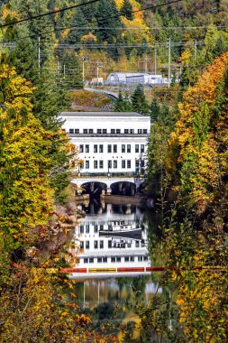 Steve Gölü 'nün eteğindeki eski elektrik santrali müzeye dönüştürüldü. Dik kıyıları olan bir nehir ladin ormanlarıyla kaplanmış ve arkasında elektrik santrali olan nehirde küçük bir tekne.