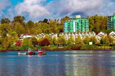 İki römorkör kıyı boyunca ilerliyor. Fraser Nehri 'nin kıyısında sakin bir yerde, binaların önünde park yeri, sonbahar renklerine boyanmış ağaçlar, bulutlu gökyüzü.