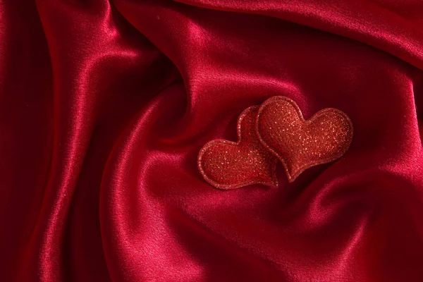 Dos corazones sobre un fondo de tela satinada con pliegues en rojo — Foto de Stock