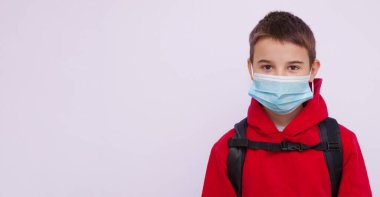 Sırtında sırt çantası olan okul çocuğu. Üzerinde sahte uzay olan bir tıbbi maske pankartı var.