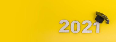 Mezuniyet 2021 ahşap numara 2021 sarı arka plan görünümlü mezuniyet şapkası giyiyor. Pankart