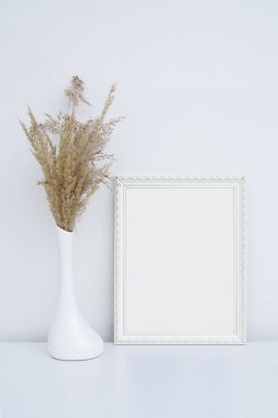 Beyaz fotoğraf çerçevesi, içinde vazo ve pampa otları olan beyaz bir iç mekan.