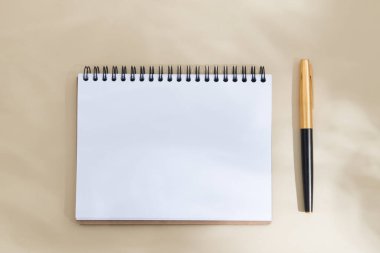 Üst görünüm boş defter sayfası ve biege arkaplanı üzerinde gölgeli bir kalem