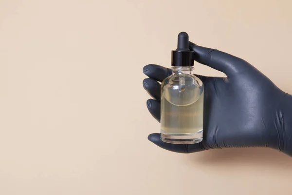 Een vrouw in een zwarte medische handschoen houdt een glazen druppelflesje vast. Kopieerbasis Stockfoto