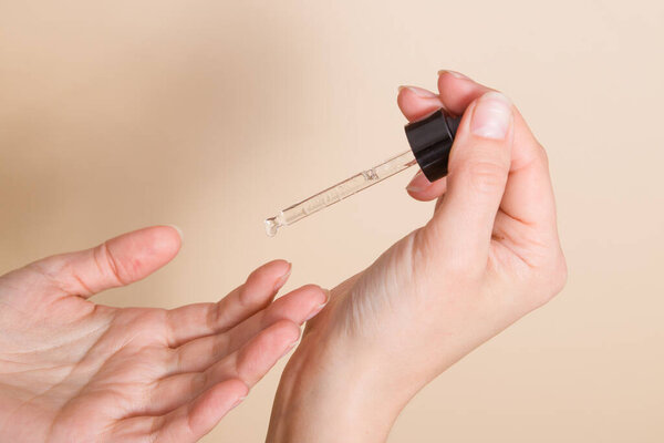 Женская рука держит стеклянную капельницу и капает масло на палец. Применение медицинского или косметического масла