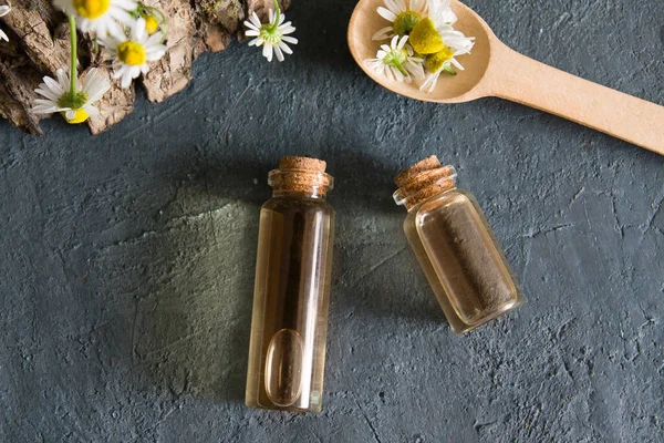 Concept de cosmétiques naturels. Bouteilles avec de l'essence et de la camomille plat posé sur un fond sombre — Photo