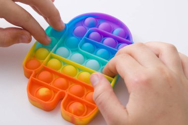 Çocuk ellerini gökkuşağı silikon oyuncağıyla kapatın anti-strese sokun, beyaz arka planda üstten bakın. Popüler çocuk oyuncağı