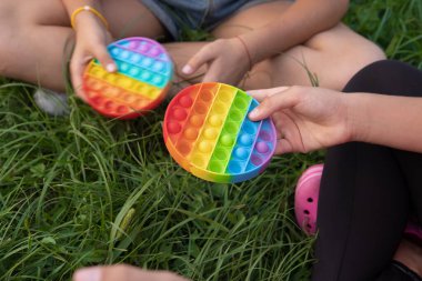 Kızlar yeşil çimenlerde popüler pop-it oyuncaklarıyla renkli silikon dokunuşlar yaparlar.