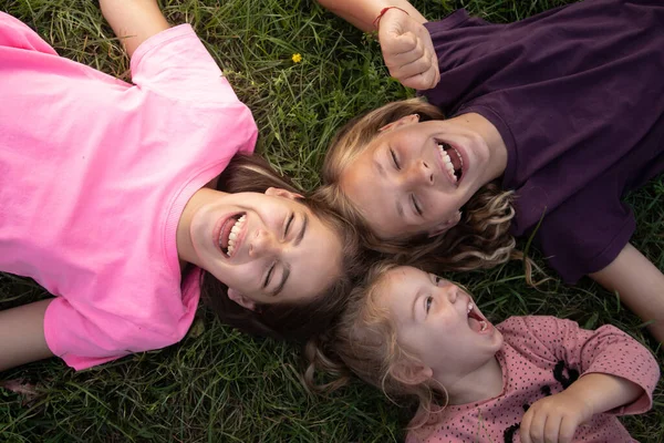 Вид сверху на трех смеющихся девочек, лежащих на траве снаружи. Беззаботное счастливое детство — стоковое фото