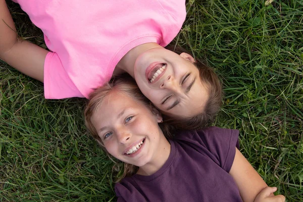 Вид сверху на двух девочек, смеющихся, лежа на траве снаружи — стоковое фото