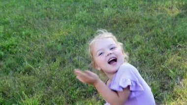 Şirin küçük kız. 3 yaşında, kıvırcık saçlı. Yeşil doğal bir arka planda at kuyruğu takmış.