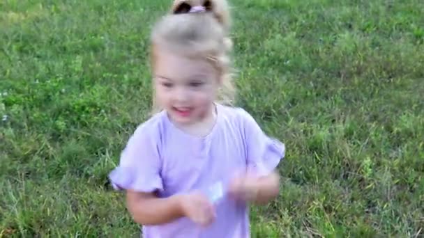 Linda niña de 3 años con el pelo rizado reunidos en una cola de caballo sobre un fondo verde natural — Vídeos de Stock