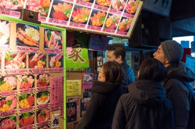 Tokyo, Japonya - 22 Ocak 2016: Tokyo, Japonya 'daki ünlü Tsukiji pazarında bir deniz ürünleri restoranının tekliflerine bakan turistler. 
