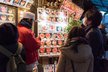 Tokyo, Japonya - 22 Ocak 2016: Tokyo, Japonya 'daki ünlü Tsukiji pazarında bir deniz ürünleri restoranının tekliflerine bakan turistler. 