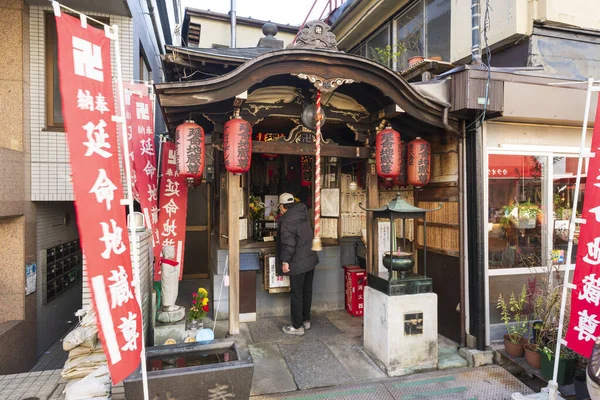 日本东京 2016年1月9日 一名日本男子在烟中银座地区的一个小街道神龛边吹点蜡烛 它是东京为数不多的几个有着低劣气氛的地区之一 低劣的氛围让人想起了过去十年的东京 免版税图库图片