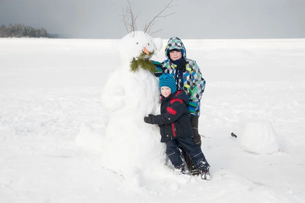 Children near the funny snowman on the ice large lake. — Stock Photo, Image