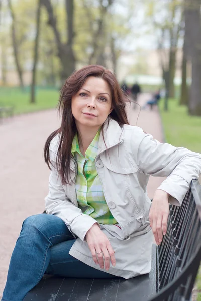 Vacker kvinna sitter på en bänk i vår Park — Stockfoto