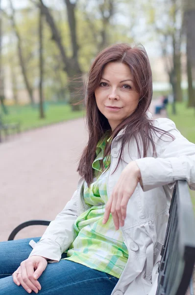 Vacker kvinna sitter på en bänk i vår Park — Stockfoto