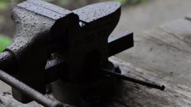 Yağmur damlalarıyla kaplı eski demir kıskaçlar, ahşap masaya yakın plan.