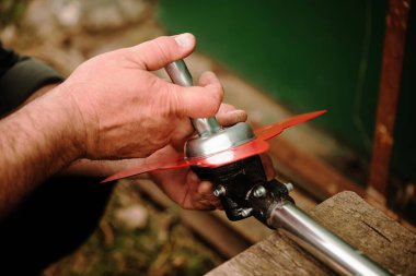 farmer prepares grass mower for work on farmland soil in spring