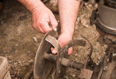 farmer prepares grass mower for work on farmland soil in spring