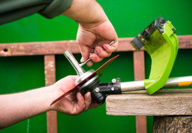farmer prepares grass mower for work on farmland soil in spring