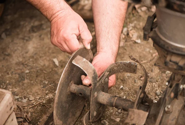 farmer prepares grass mower for work on farmland soil in spring