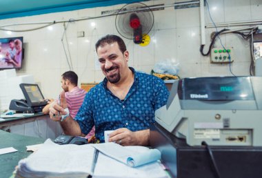 Deniz ürünleri restoranı satıcısı tezgahın arkasındaki kasada gülümsüyor.