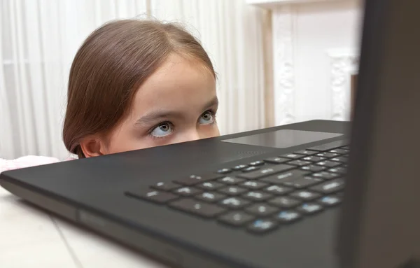 A rapariga escondeu-se debaixo da mesa, a olhar para um computador — Fotografia de Stock