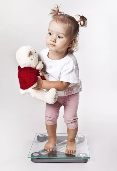 Little girl with toy weighed on the scales — Stock Photo, Image