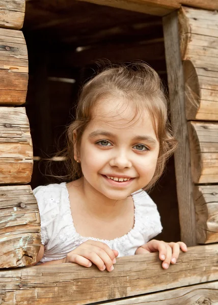 Весела дівчина виглядає з віконного отвору дерев'яного будинку — стокове фото