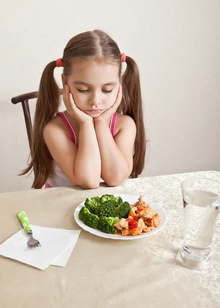 A menina olha indiferentemente para o prato com carne e brócolis — Fotografia de Stock