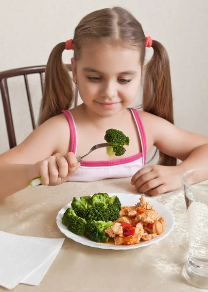 Девушка сидит за столом и смотрит на еду — стоковое фото
