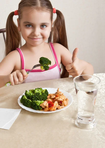 Menina feliz sentada à mesa e mostra o polegar — Fotografia de Stock