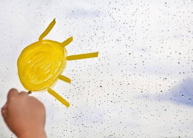 A child draws the sun on glass during rain against the sky clipart