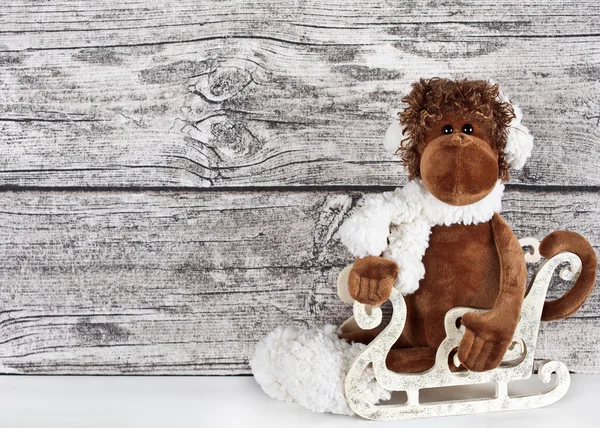 Um macaco de brinquedo em um trenó em um fundo de madeira branco — Fotografia de Stock